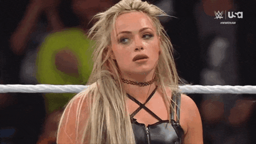 a woman is standing in a wrestling ring wearing a choker and looking at the camera .
