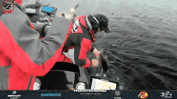 a man in a red and gray jacket is fishing on a boat with a humminbird logo in the background