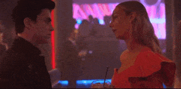 a woman in a red dress is standing in front of a man in a dark room .
