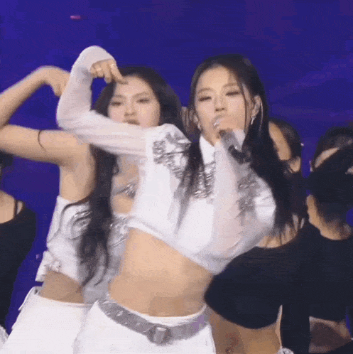 a woman in a white crop top is singing into a microphone on stage .