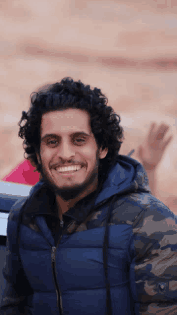 a man with curly hair and a blue jacket smiles