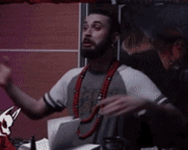 a man with a beard is wearing a gray shirt and red beads