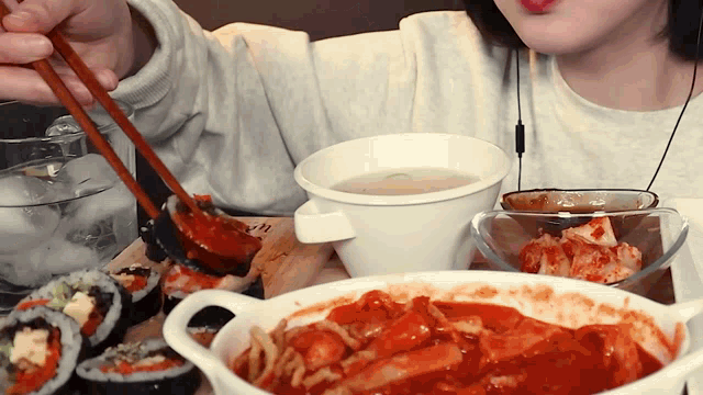 a woman is eating sushi and a bowl of soup with chopsticks