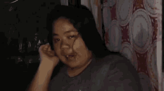 a woman with blood on her face is sitting in front of a curtain and making a funny face .