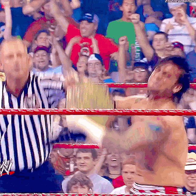a referee in a striped shirt stands in a wrestling ring with a shirtless wrestler