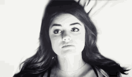 a black and white photo of a young woman with long hair making a funny face .
