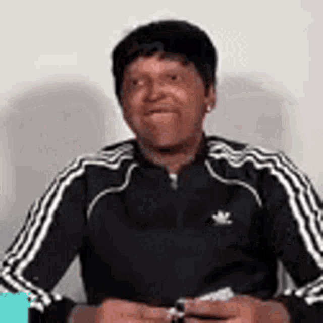 a man in a black adidas jacket is sitting at a table holding a ring .