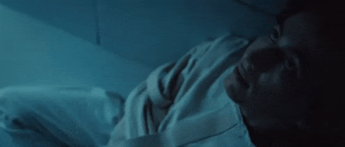a man in a white shirt is laying on the floor in a dark room looking up .