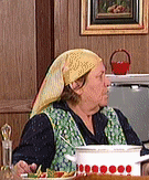 a woman wearing a yellow head scarf is sitting at a table with a pot of food .