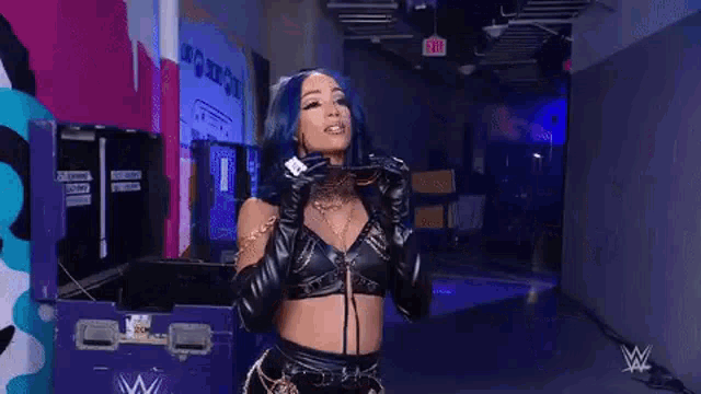 a woman with blue hair is wearing sunglasses and gloves while standing in a dark room .