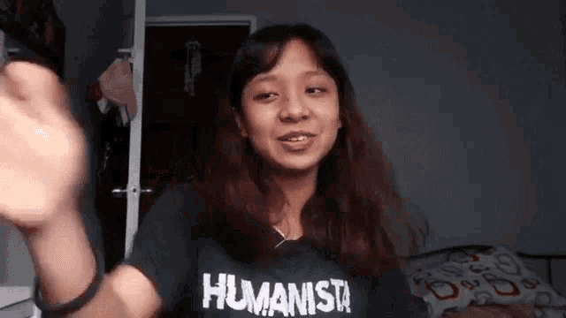 a woman wearing a black shirt that says humanista is smiling and waving her hand .