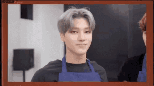 a young man wearing a blue apron is standing in a room .