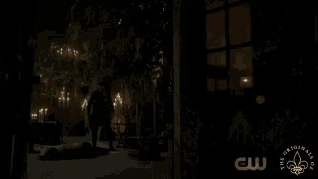 a man stands in front of a row of lit candles with a logo for the originals in the corner