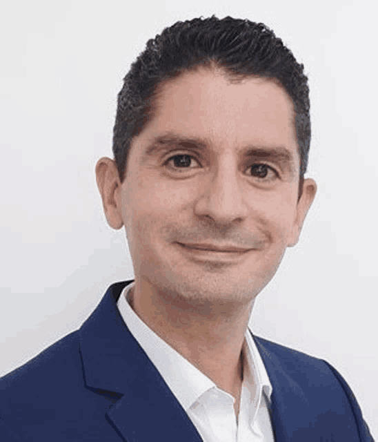 a man in a blue suit and white shirt is smiling and looking at the camera .