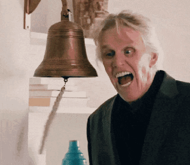 a man in a suit is screaming in front of a brass bell
