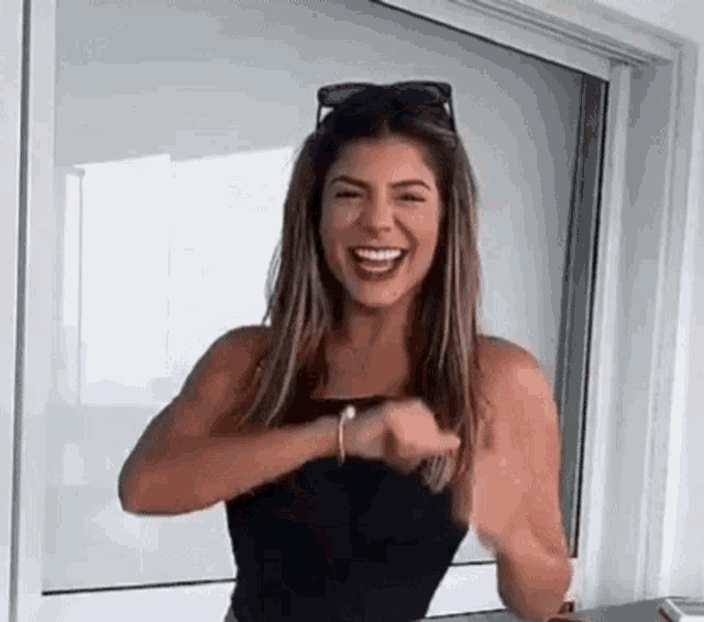 a woman in a black tank top is standing in front of a window .
