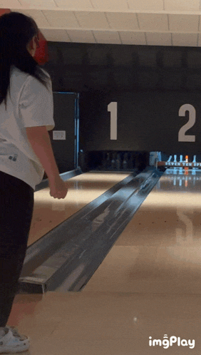 a girl playing bowling with the number 12 on the wall behind her