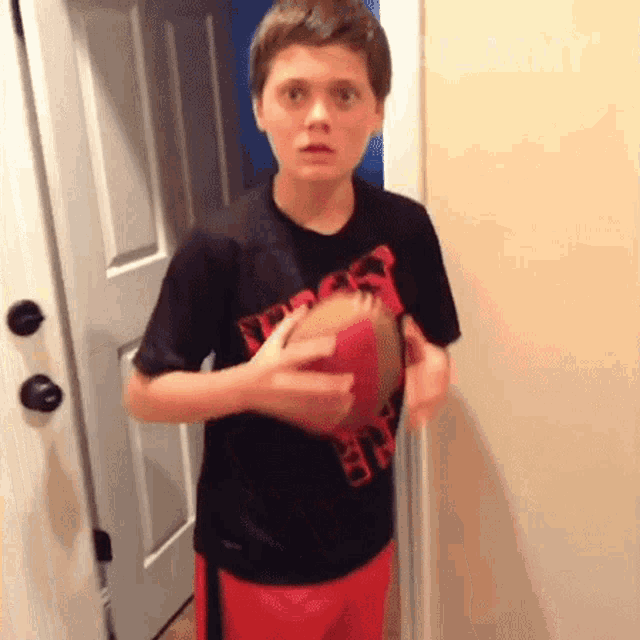 a young boy in a black shirt is holding a red basketball in his hands .