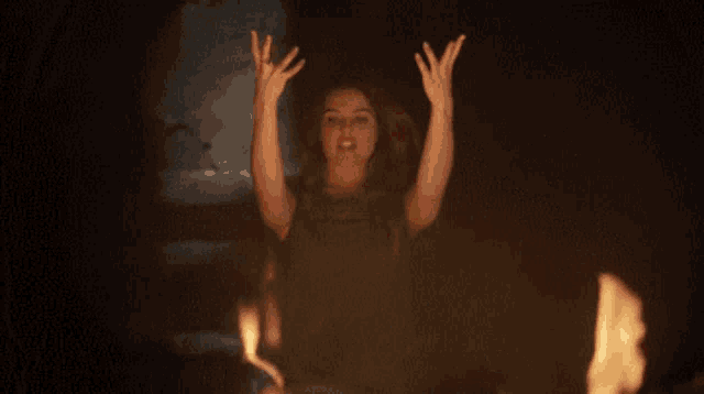 a woman is standing in front of a fire with her hands up