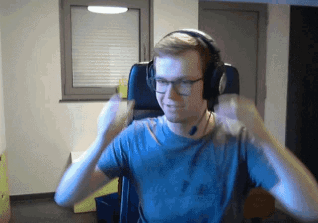 a man wearing headphones and glasses is sitting in a chair with his hands in the air