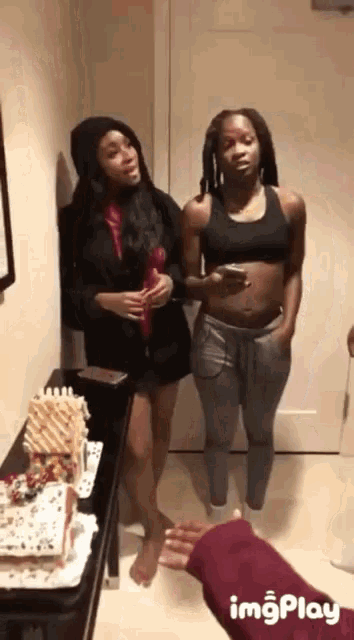 two women standing next to each other in a room with a gingerbread house in the background