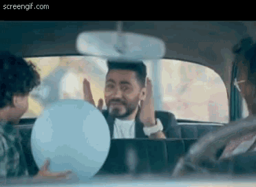 a man with a beard is holding a blue balloon in the back seat of a car .