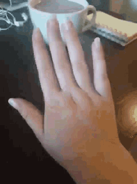 a woman 's hand reaches out towards a cup of coffee