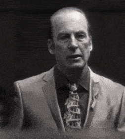 a man in a suit and tie is standing in a dark room and looking at the camera .