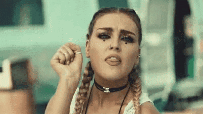a woman with braids is making a funny face while wearing a choker and a ring .