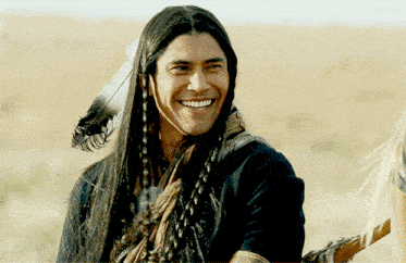 a man with long hair and feathers on his head smiles for the camera