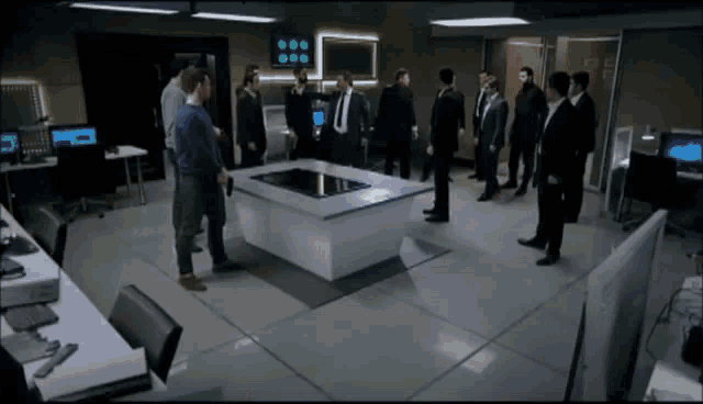 a group of men are standing around a table with a touchscreen