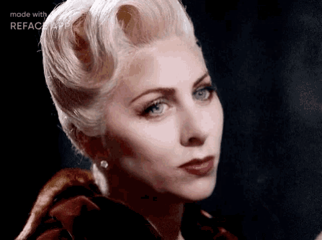 a woman with blonde hair and blue eyes is wearing a red coat and earrings .