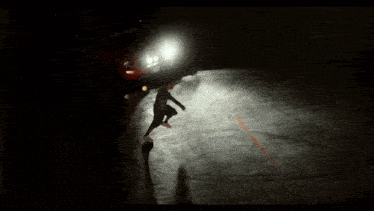 a person riding a skateboard in a dark parking lot with a car behind them