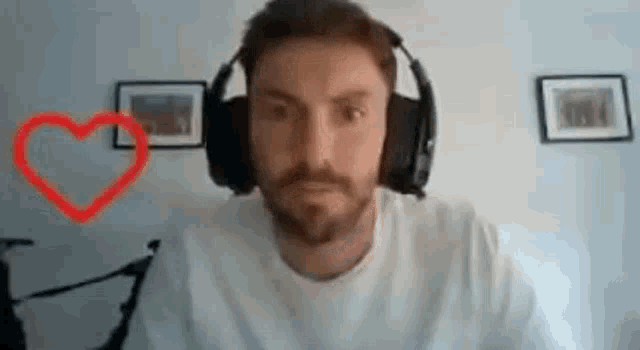 a man with a beard is wearing headphones and looking at the camera with a heart drawn on the wall behind him .