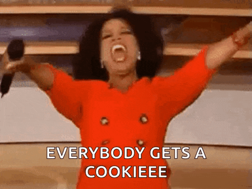 oprah winfrey is holding a microphone with her arms outstretched and says everybody gets a cookieeee .