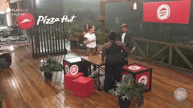 a group of people are standing around a table in a room with a pizza hut sign .