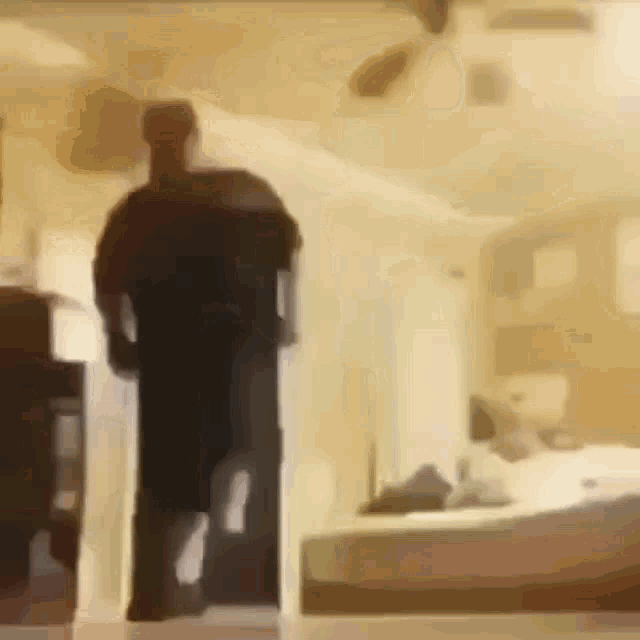 a blurry picture of a man standing in a room with a bed in the background .