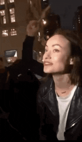 a woman in a leather jacket is sitting in a dark room with a man holding a glass of wine .