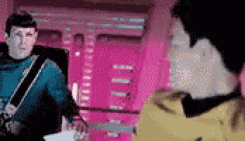 two men are standing next to each other in a room and talking .