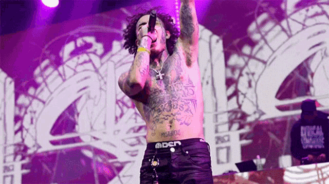 a shirtless man with tattoos is singing into a microphone on a stage