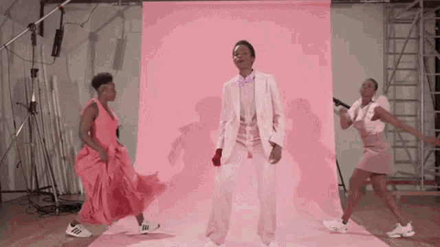 a man in a suit and tie is dancing with two women in pink dresses