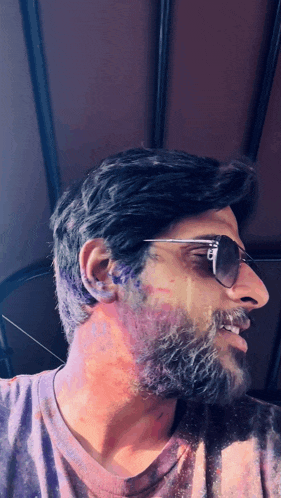 a man with a beard wearing sunglasses and a purple shirt is covered in purple powder