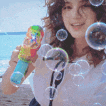 a woman blowing soap bubbles on the beach with a colorful toy