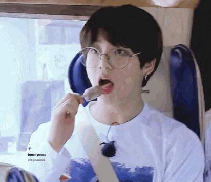 a young boy wearing glasses is eating an ice cream cone while sitting on a bus .
