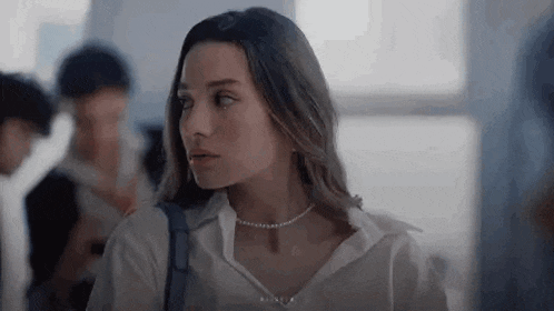 a woman wearing a pearl necklace and a white shirt is standing in a room .
