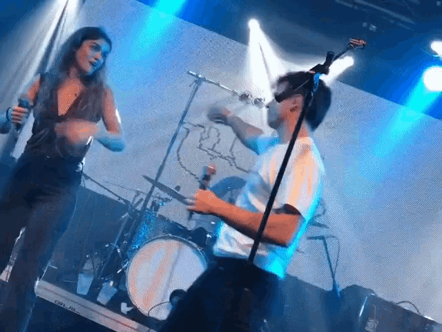a woman singing into a microphone while a man plays a drum