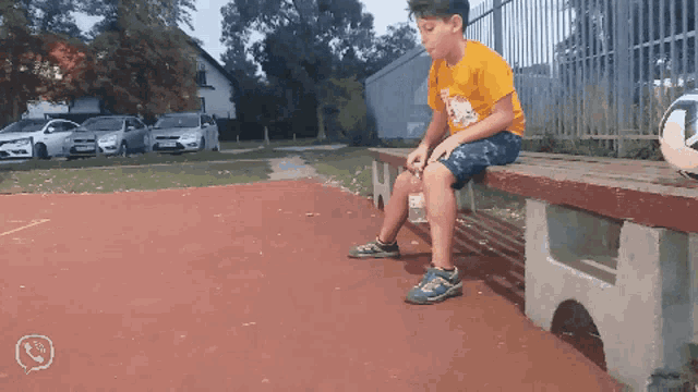 a boy sits on a bench with a soccer ball in the background