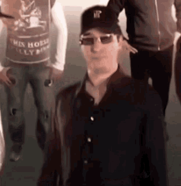 a man wearing a hat and sunglasses is standing in a crowd of people .