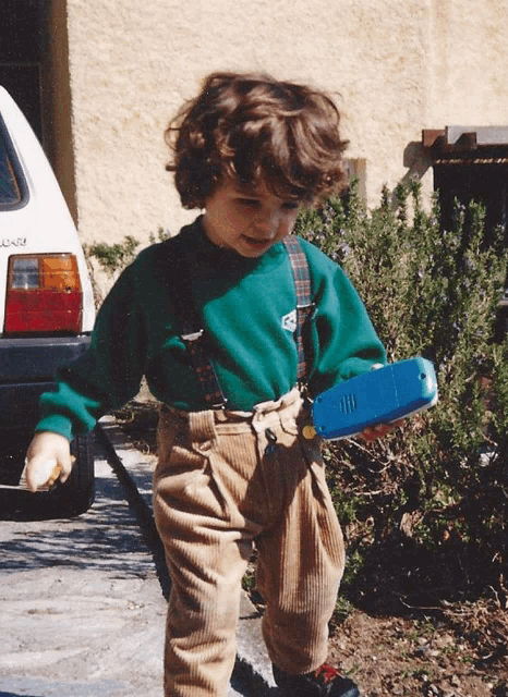 a young boy holding a blue toy in front of a car that says laguna on the back