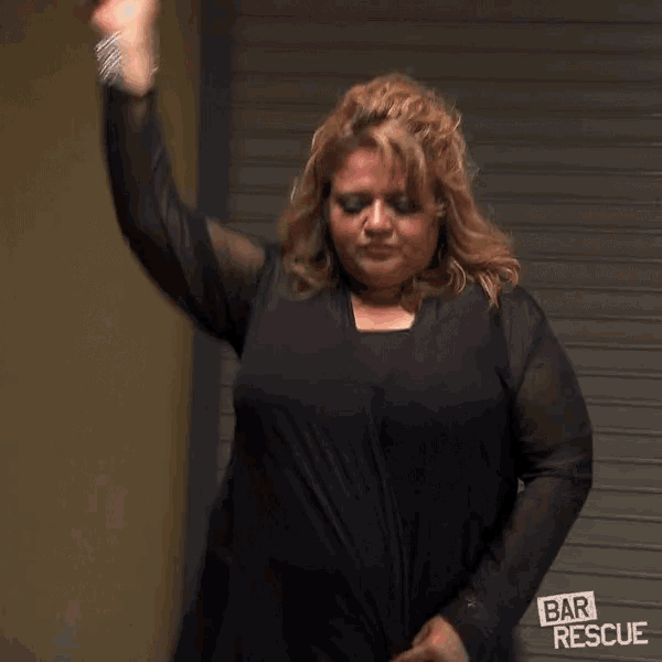 a woman in a black dress is dancing in front of a bar rescue sign